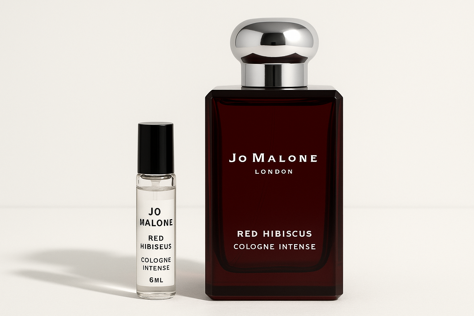 Amostra de Jo Malone Red Hibiscus Cologne Intense de 6 ml ao lado de um frasco de perfume de 100 ml de Jo Malone Red Hibiscus Cologne Intense, com escrita branca no frasco vermelho escuro